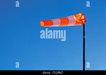 Orange and white windsock blows against a blue sky. Stock Photo