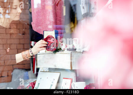 A mature woman rearranging the window display of a gift and craft store. Stock Photo