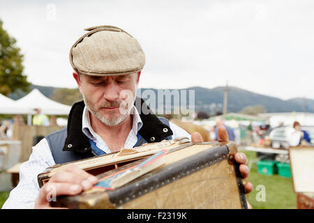 Man wearing a flat cap looking at a vintage suitcase at a flea market. Stock Photo