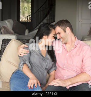 Smiling man and woman sitting on a sofa, hugging, and looking at each other. Stock Photo
