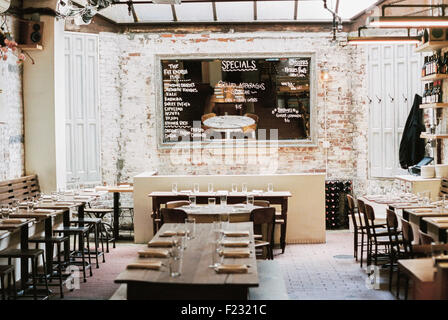 A restaurant with long narrow tables and chairs laid for a meal. A large chalk menu board. Stock Photo