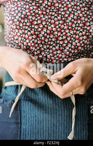 A woman tying the tapes of an apron around her waist. Stock Photo