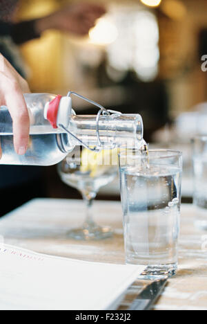 A hand pouring water from a bottle with a clip top into a glass. Stock Photo