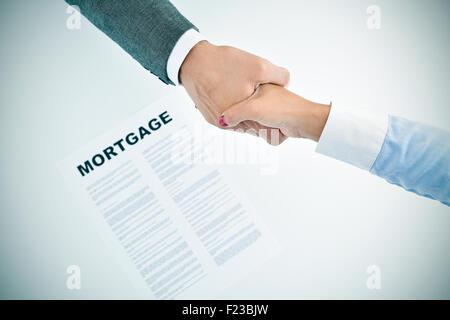 closeup of a young man and a young woman shaking hands above a table with a mortgage loan document, slight vignette added Stock Photo