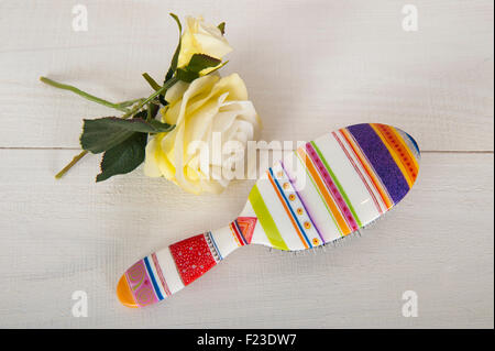 A brightly coloured hairbrush on a white background with two yellow roses flowers Stock Photo
