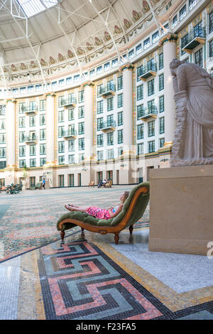 Caucasian girl wearing a pink dress reclines on a velvet chaise in the six story atrium at West Baden Springs Resort Stock Photo