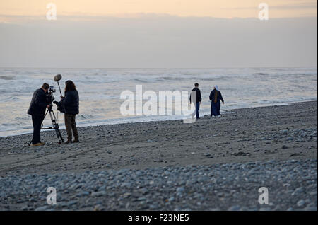 GREYMOUTH, NEW ZEALAND, JULY 30, 2015: A cameraman and sound recordist at work on a New Zealand beach at sunset. Stock Photo