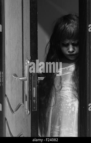 A creepy little girl staring from behind the door Stock Photo