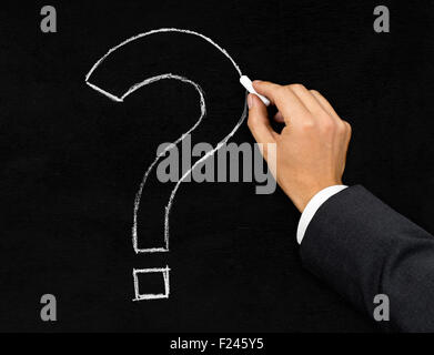 Male businessman drawing question mark with chalk on blackboard background Stock Photo