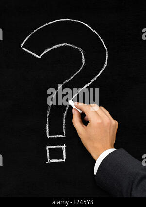 Male businessman drawing question mark with chalk on blackboard background Stock Photo