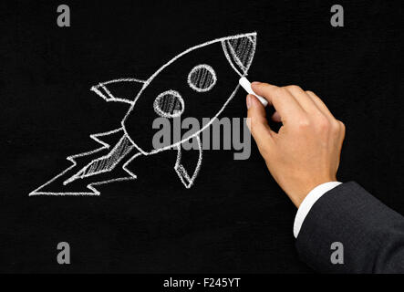 Businessman drawing cartoon rocket with chalk on blackboard background - innovation, startup or idea concept Stock Photo