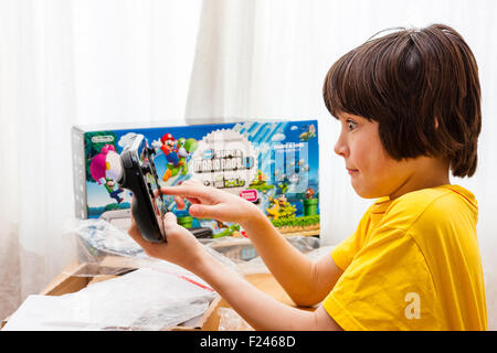 Caucasian male child, boy, 11-13 year old, holding in both hands a Wii U Nintendo Console just after taking it out of the box, which is next to him. Stock Photo