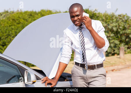 young African man calling for assistance with his car broken down by the roadside Stock Photo