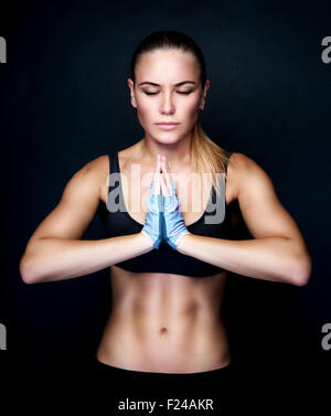 Beautiful woman meditating in the studio, doing yoga exercises over black background, sportive lifestyle, healthy active life