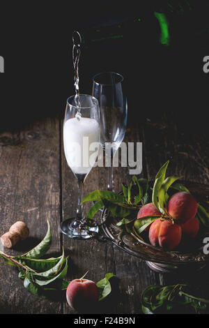 Peaches on branch with leaves in vintage plate and two glass of champagne with cork over old wooden table. Champagne pouring fro Stock Photo