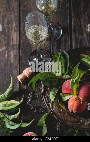 Peaches on branch with leaves in vintage plate and two glass of champagne with cork over old wooden table. Dark rustic style. Stock Photo