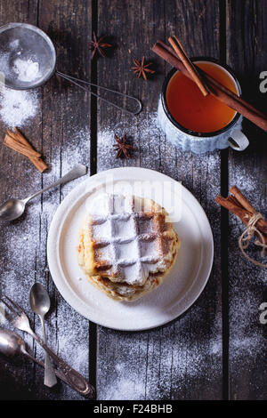 White plate with homemade belgian waffles with sugar powder and vintage cup of tea with cinnamon stick at background. Teaspoons Stock Photo