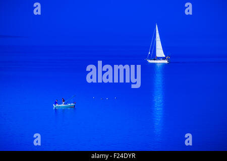 Small fishing boat and sailing boat meet in the blue sea. Stock Photo