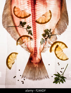 Pink translucent headless fish with bones, tail and fins on light table with lemon and parsley Stock Photo