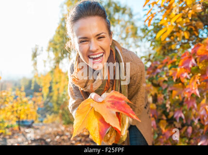 Laughing young woman holding colorful autumn leafs in city park Stock Photo