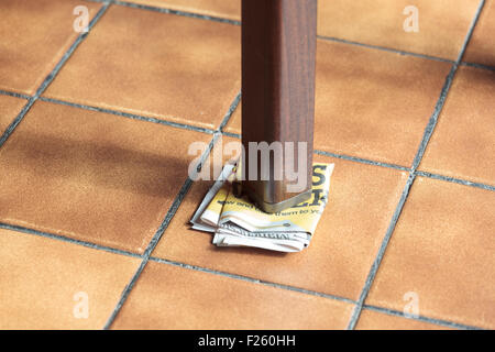 Leg of a wobbly table supported by folded paper Stock Photo