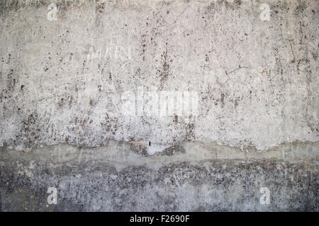 Weathered, aged and cracked gray stone wall with names scratched on it. Stock Photo