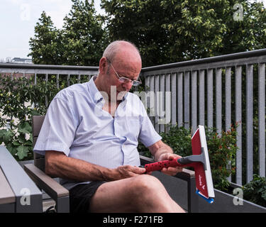 Senior man sitting on apartment balcony looking at window cleaner Stock Photo
