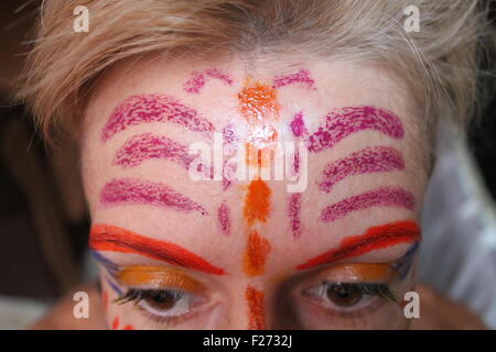 forehead of young white girl painted with symbol of dragonfly on skin Stock Photo