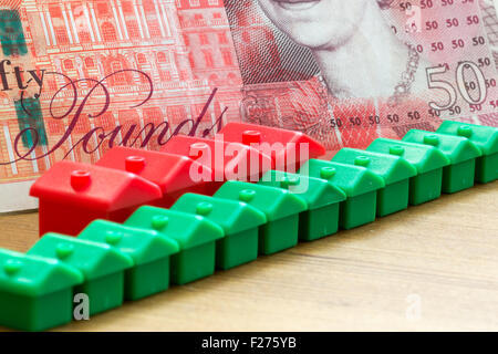 Green and red imitation plastic model houses form a dynamic diagonal row with a single British fifty pound bank note in the back Stock Photo