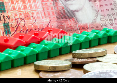 Green and red imitation plastic model houses form a dynamic diagonal row with a single British fifty pound bank note in the back Stock Photo