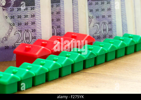 Green and red imitation plastic model houses form a dynamic diagonal row with piles of British twenty pound bank notes in the ba Stock Photo