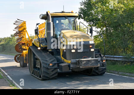 Farmer driving Caterpillar challenger tractor and folded disc harrow taking up most of the width in a narrow country lane rural Essex England UK Stock Photo