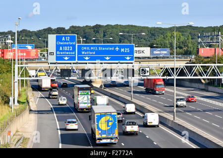 Transport options M25 motorway railway bridge & container freight train above road traffic blue road signs for junction 28 Brentwood Essex England UK Stock Photo