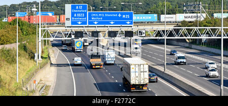 Container freight train crossing railway bridge above road traffic at junction 28 of  M25 motorway at Brentwood Essex England UK blue road sign gantry Stock Photo