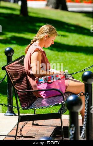Young woman sits on street bench seat eating a snack at lunchtime in Madison Wisconsin Stock Photo