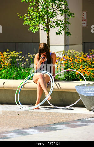 A college girl answering a text message on her cell phone and taking a break from practicing with Hoola-Hoops in Madison WI Stock Photo