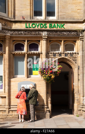 A couple using the ATM cash machine outside Lloyds bank; Glastonbury branch, High St, Glastonbury town, Somerset England UK Stock Photo