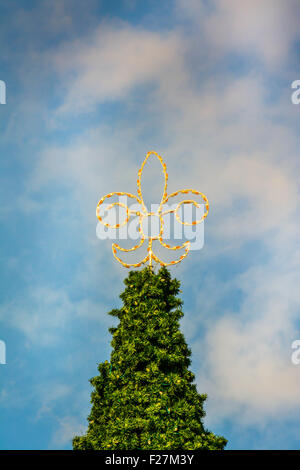 Fleur de Lis decoration with lights sits atop an evergreen tree strung with more lights with cloudy blue sky in New Orleans LA Stock Photo