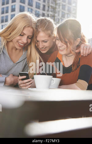 Three friends text messaging at sidewalk cafe, Munich, Bavaria, Germany Stock Photo