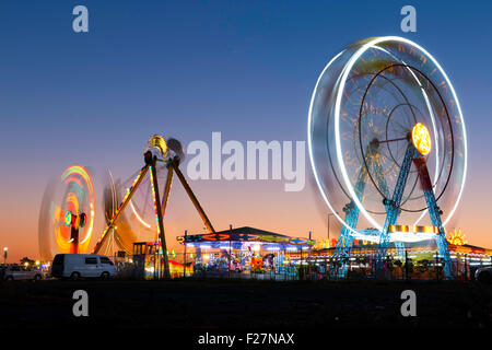 Colorful carnival Ferris wheel and gondola spinning in motion blurred at twilight in an amusement park Stock Photo