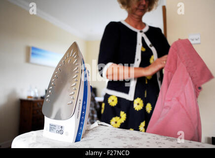 Middle aged woman using Russell Hobbs steam iron pressing or ironing clothes at home Stock Photo