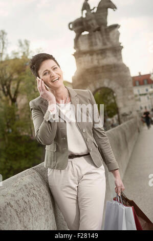 Mature woman phoning in city with shopping bags, Bavaria, Germany Stock Photo