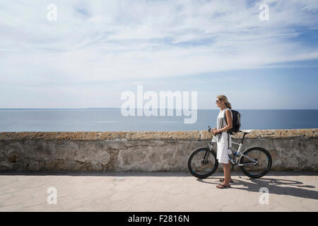 Side profile of mature woman standing with mountain bike on harbor wall, Gallipoli, Puglia, Italy Stock Photo