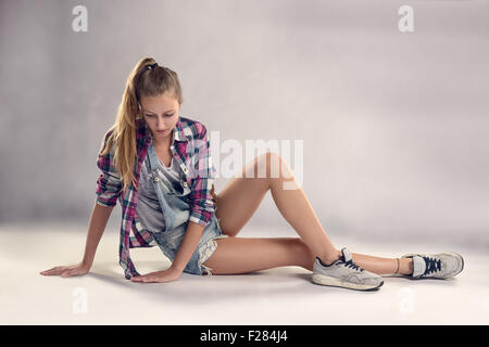 Stylish Young Modern Female Dancer Sitting on the Floor, with a Thoughtful Facial Expression, Against Gray Wall Background. Stock Photo
