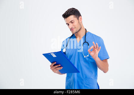 Portrait of a happy male doctor reading clipboard and showing ok sign isolated on a white background Stock Photo