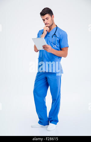 Full length portrait of a thoughtful male doctor holding tablet computer isolated on a white background Stock Photo