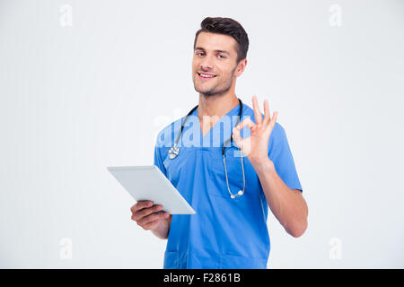 Portrait of a happy male doctor holding tablet computer and showing ok sign isolated on a white background Stock Photo