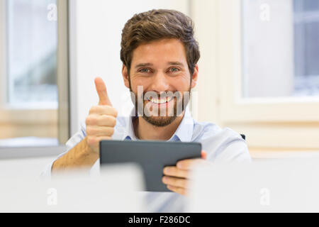 Happy businessman with thumb up in office using digital tablet Stock Photo