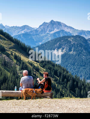 Breitenberg mountain path and senior couple with dog sitting on bench - Tannheim mountain range, near Pfronten, Bavaria, Germany Stock Photo