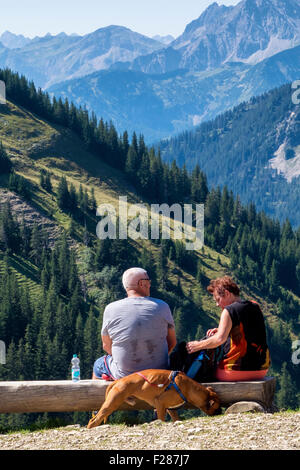 Breitenberg mountain path and senior couple with dog sitting on bench - Tannheim mountain range, near Pfronten, Bavaria, Germany Stock Photo